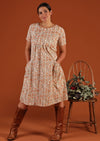 Model has hands in pockets of cream floral dress