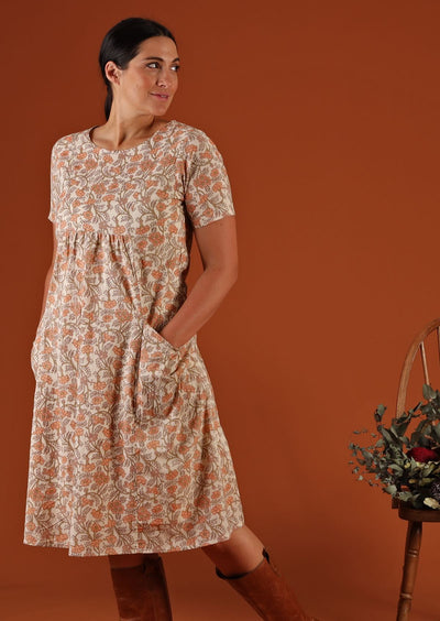 The model wears a cream floral dress  with hands in pockets