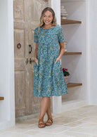 Woman standing with both the hands in pocket wears short sleeved loose fit cotton dress with round neckline.