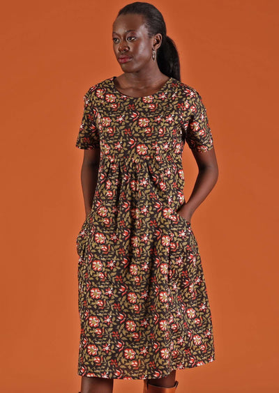 Model wears green and red on black base floral dress with pockets.