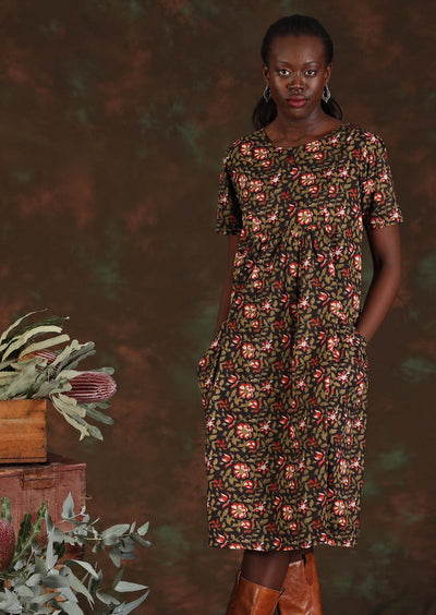 Model wears knee length floral dress with hands in pockets