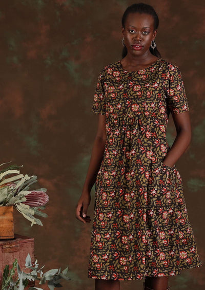 Model wears a 100% cotton knee length dress with pockets. With a green and red floral pattern on a black base.