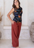 Woman stands sideways with hands in pockets, wearing relaxed-fit cotton pants in rust paired with a floral print cotton top