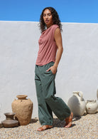 Woman wearing a pink top and green wide leg pants with little pleats at the ankle cuff to taper them in slightly