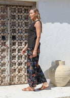 Model stands sideways wearing a sleeveless black cotton top paired with printed wide leg cotton pants featuring pleated ankles and pockets