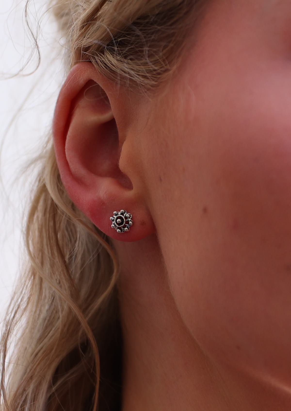 A close-up image of a person wearing sterling silver round stud earrings with an ornate pattern.