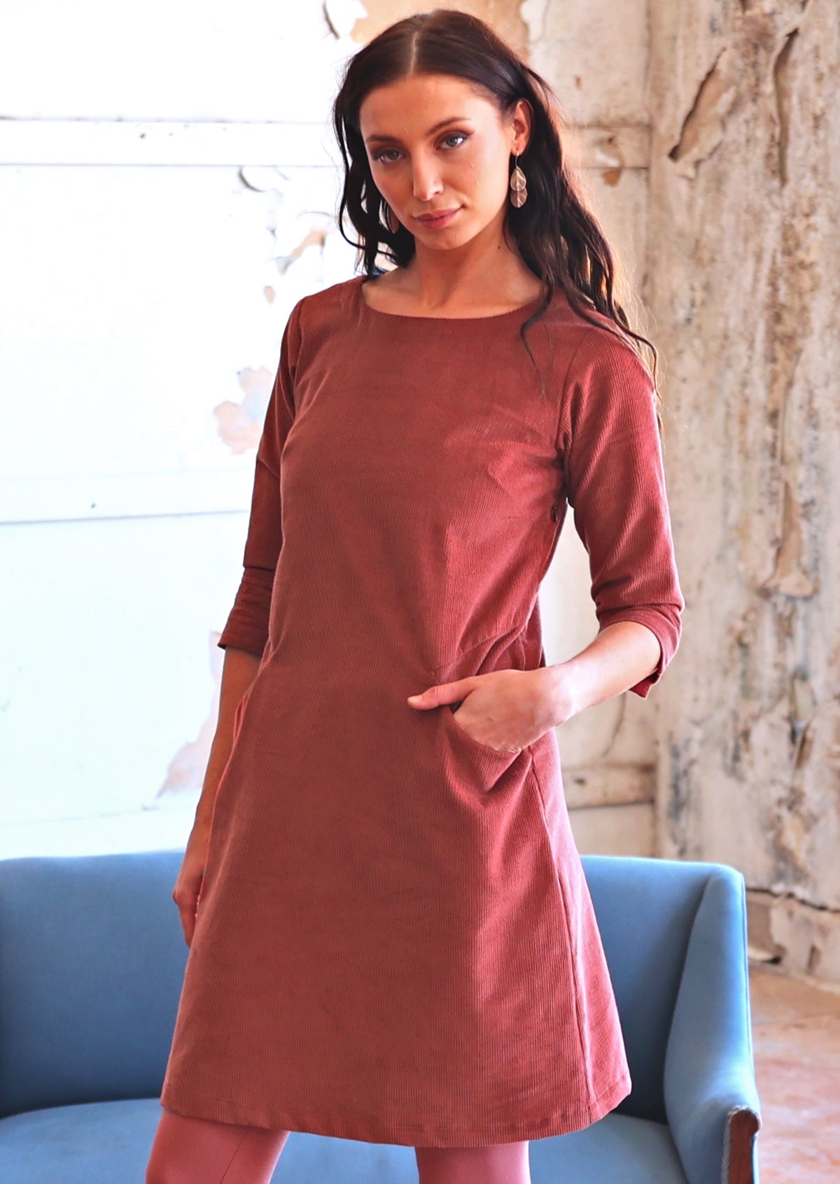 Woman in rust coloured corduroy tunic with hand in pocket
