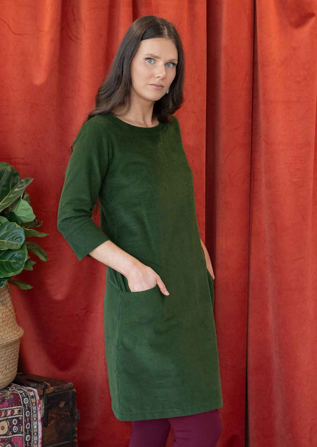 Woman wearing green corduroy A-line dress with 3/4 sleeves with hands in pockets 