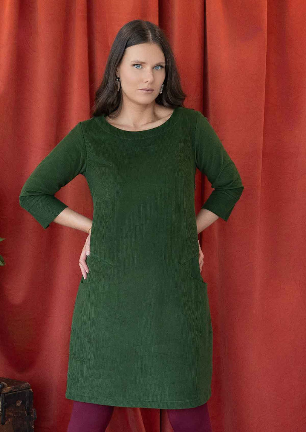 Woman wearing green corduroy A-line dress with 3/4 sleeves with hands on hips