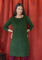 Woman wearing green corduroy A-line dress with 3/4 sleeves with hands on hips