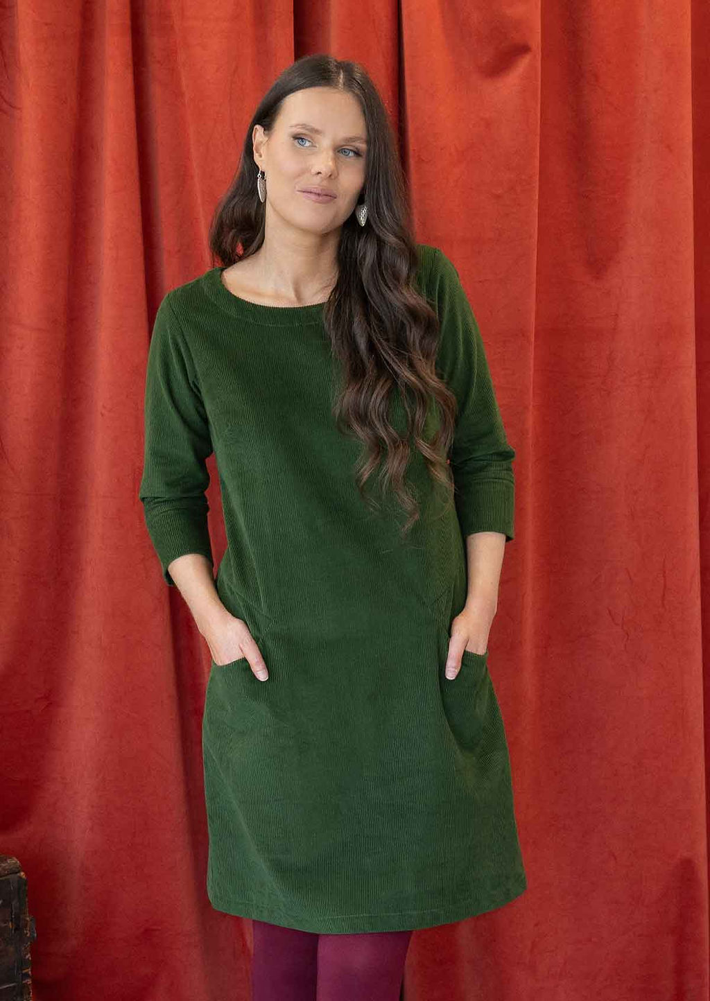 Woman wearing green corduroy A-line tunic with 3/4 sleeves with hands in pockets 