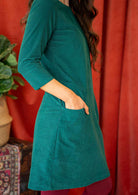 Woman wearing teal corduroy dress over pink leggings hand in pocket