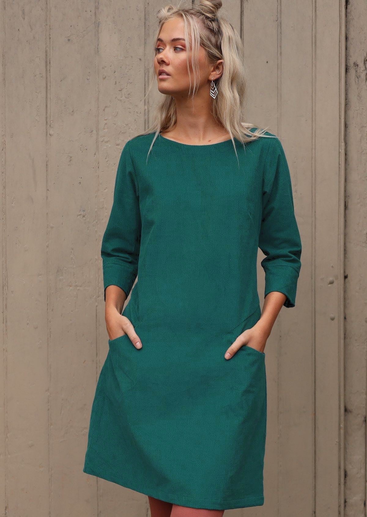 Woman with blond hair wearing Teal corduroy A-line dress with 3/4 sleeves with hands in pockets 