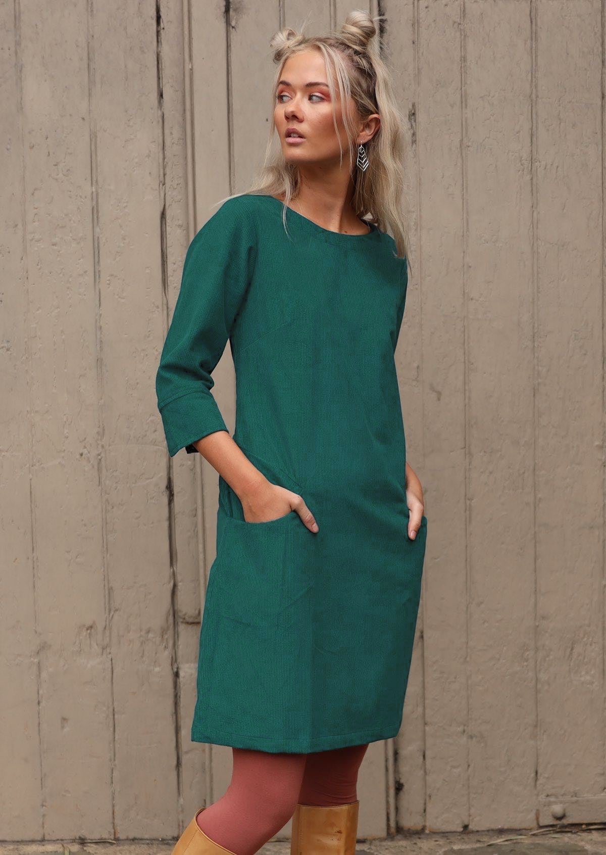 Woman with blonde hair wearing teal corduroy dress over pink leggings in front of old door