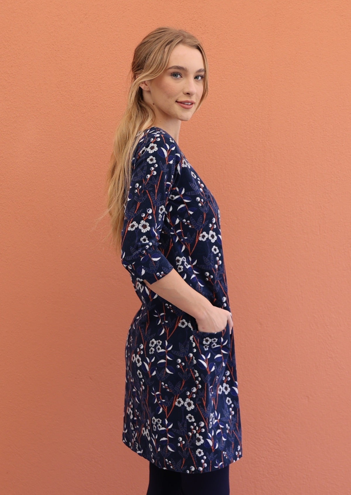Model wears cotton corduroy above knee length, A-line floral print dress with hand in pocket.
