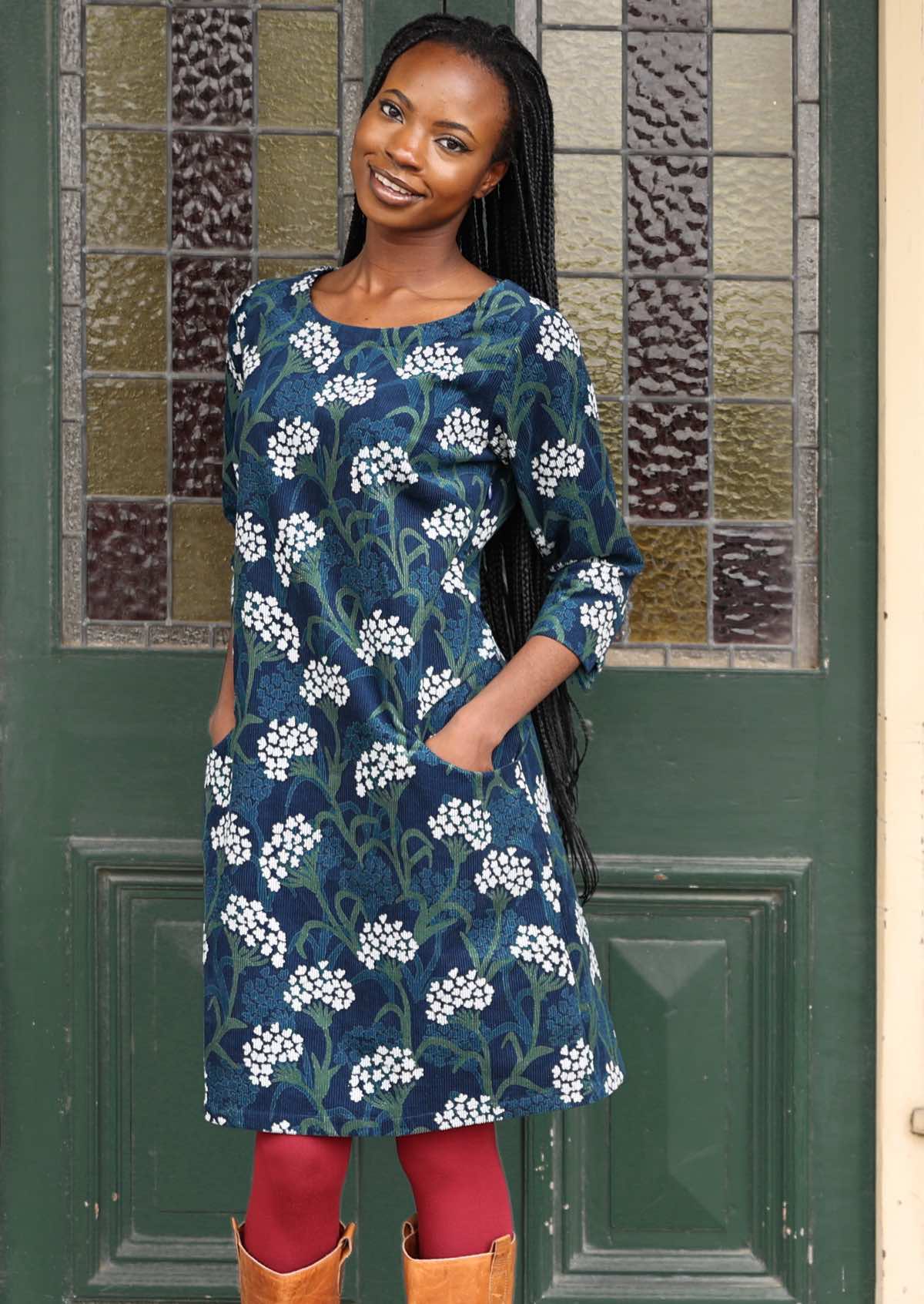 Model poses in cotton corduroy A-line above knee floral print dress with hands in pockets