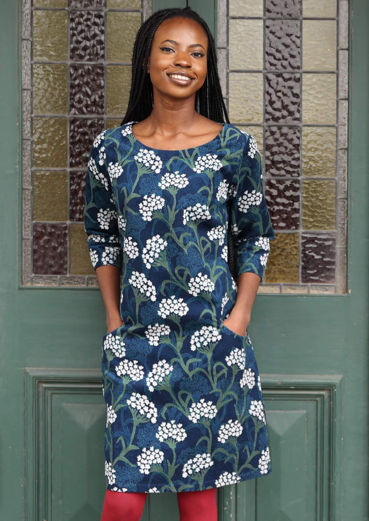 Model poses in front of door in blue, green and white floral on dark blue base cotton corduroy dress