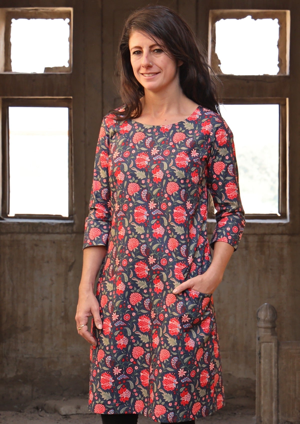 Woman with hand in pocket wearing long sleeve 100 percent cotton dress with deep blue base and raspberry red floral print 