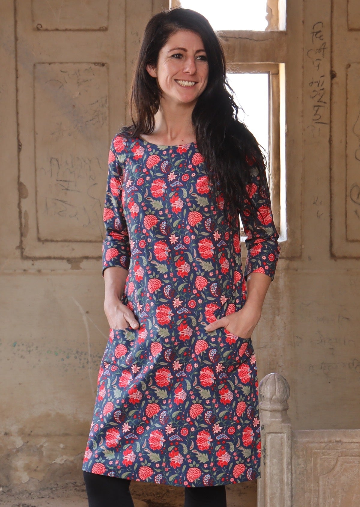 Woman with hands in pockets wearing long sleeve 100 percent cotton dress with deep blue base and raspberry red floral print 