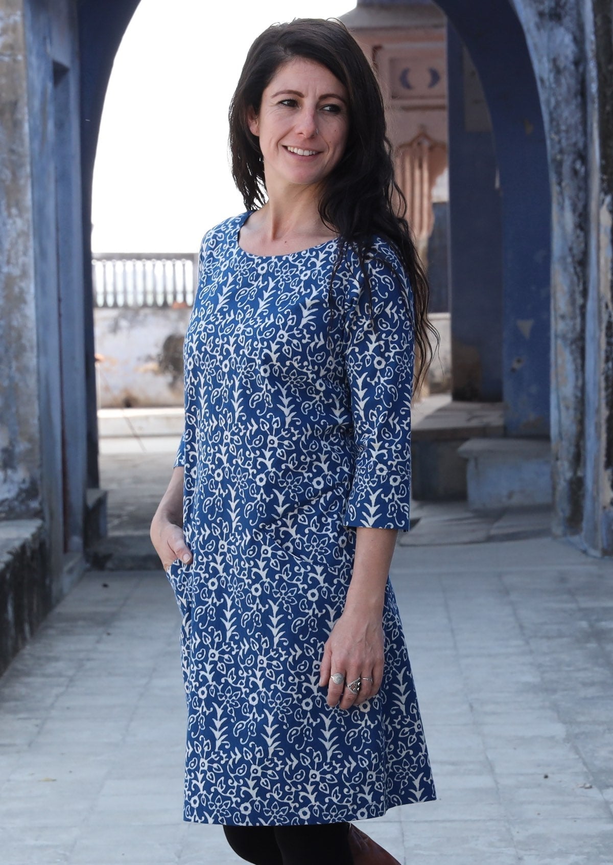 Woman standing side on with hand in pocket wearing 100% cotton blue and white dress 