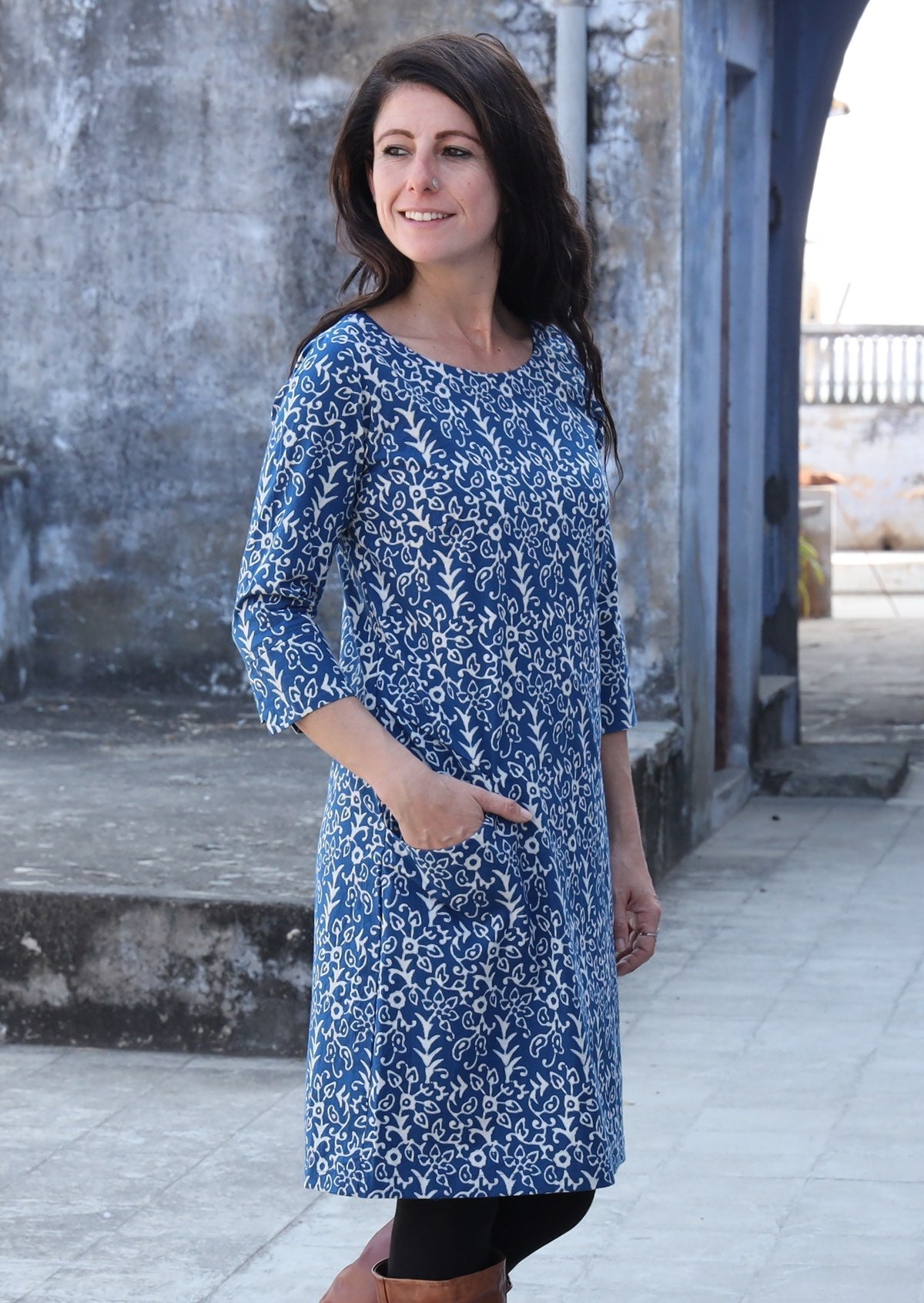 Woman standing sideways with her hand in her pocket wearing 100% cotton blue and white dress 