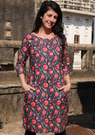 Woman with hands in pockets wearing 100 percent long sleeve cotton dress with deep blue base and raspberry red floral print 