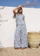 Woman in a white based blue floral cotton pant against a white wall.