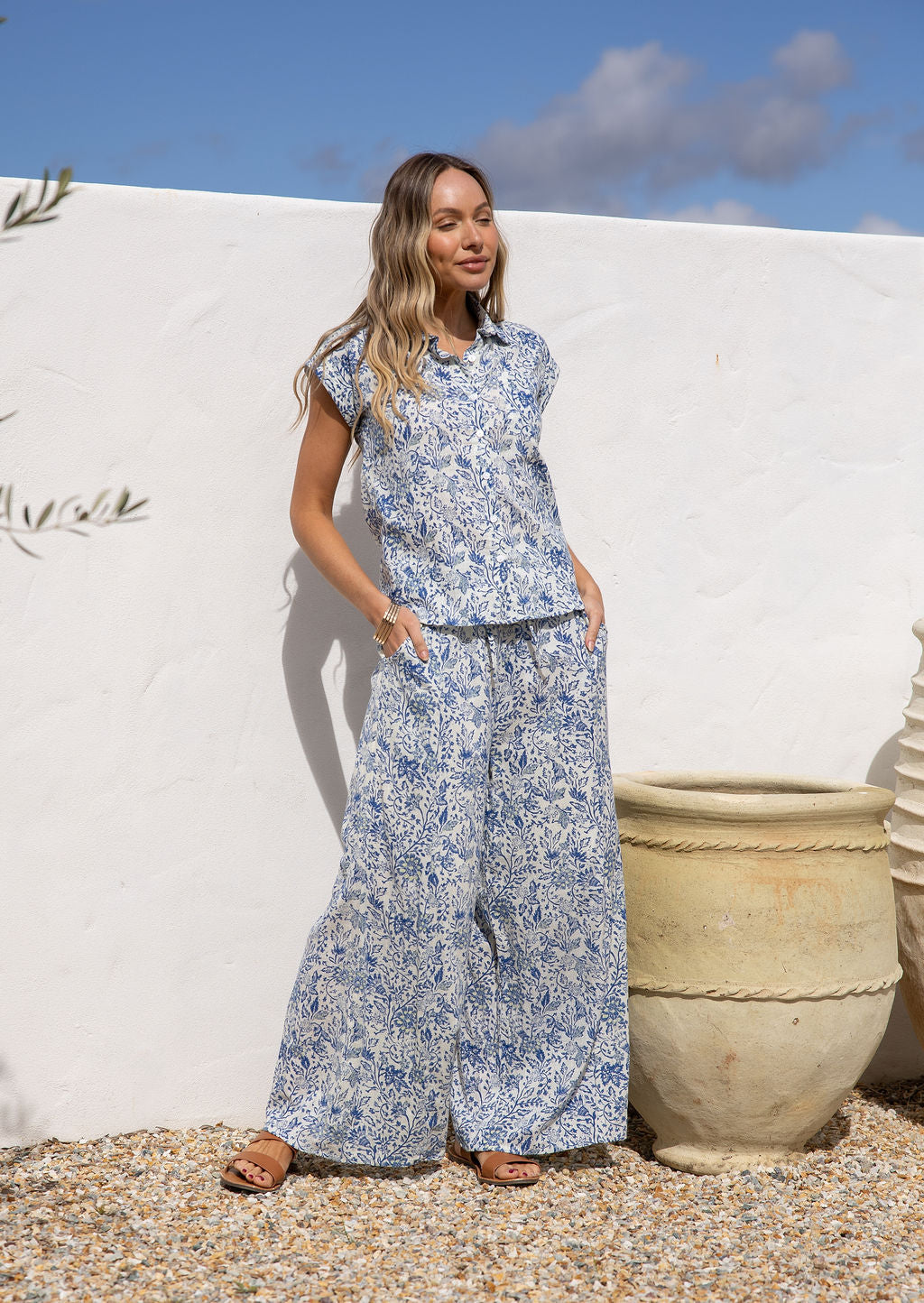Woman in a white based blue floral cotton pant wide legged against a white wall.