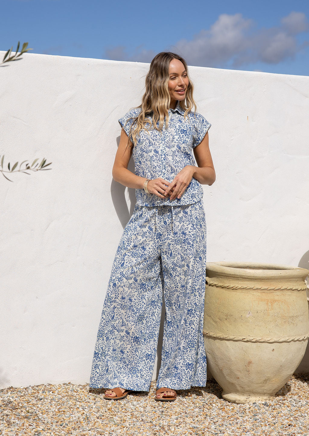 Woman in a white based blue floral print, 100% cotton pant against a white wall.