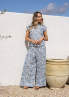 Woman in a white based blue floral print, 100% cotton pant against a white wall.