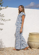 Woman in a white based blue floral cotton pant against a white wall.