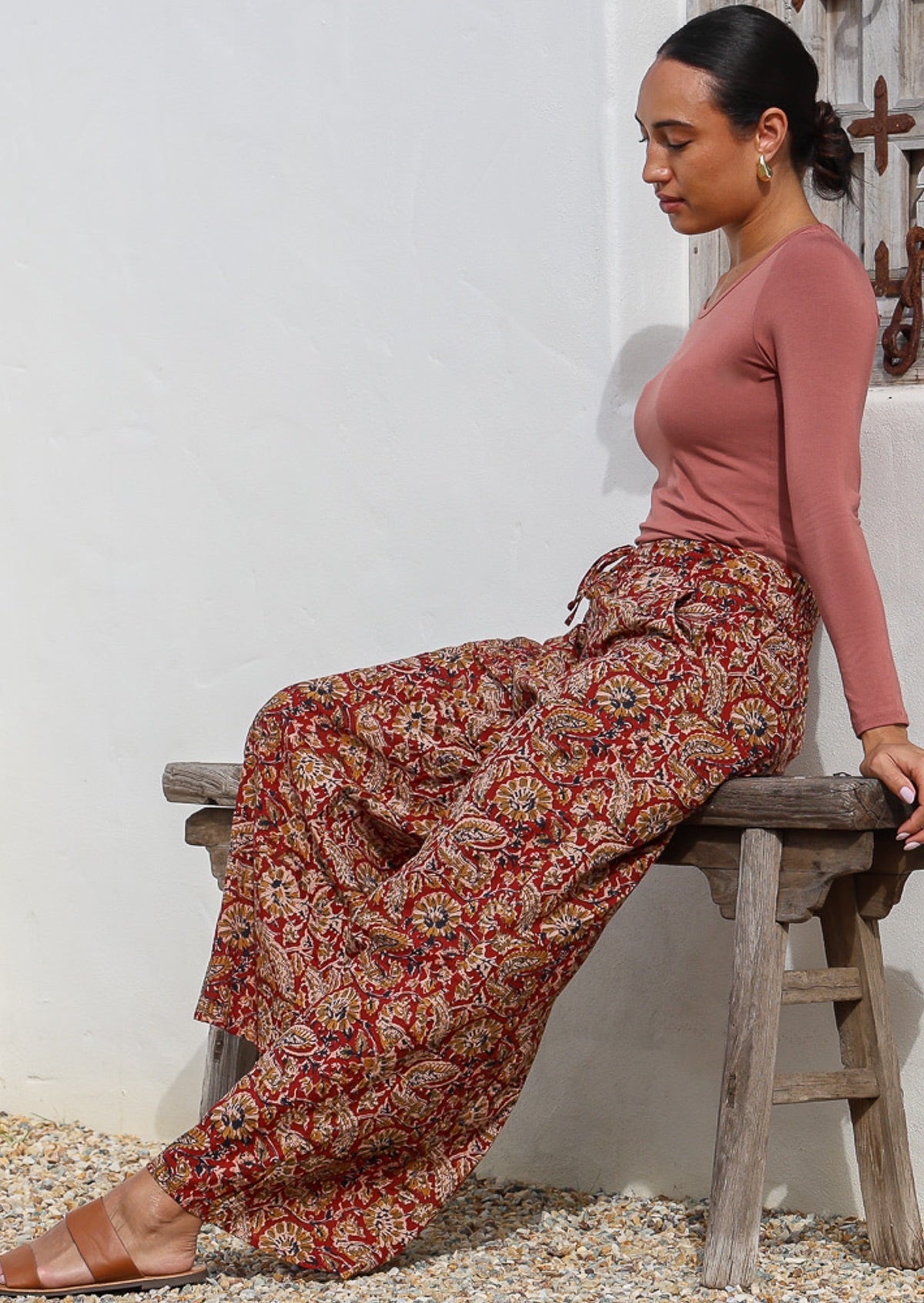 Side seated pose of model in wide leg, relaxed fit cotton pants with drawstring and pockets; paired with long sleeve rayon top in dusty rose.