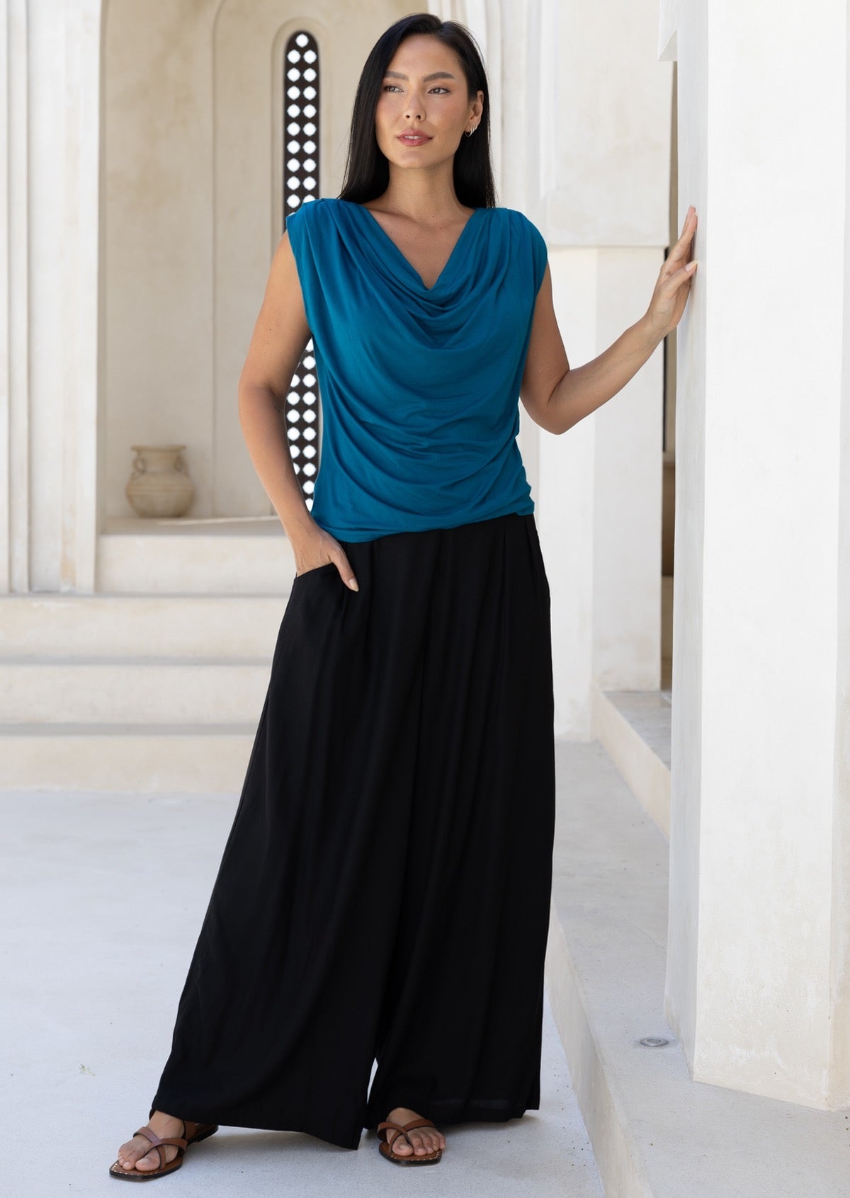 Woman wearing a blue sleeveless top paired with wide leg black rayon pants with one hand in pocket
