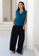 Woman wearing a blue sleeveless top and black pants standing in a bright, minimalistic room.