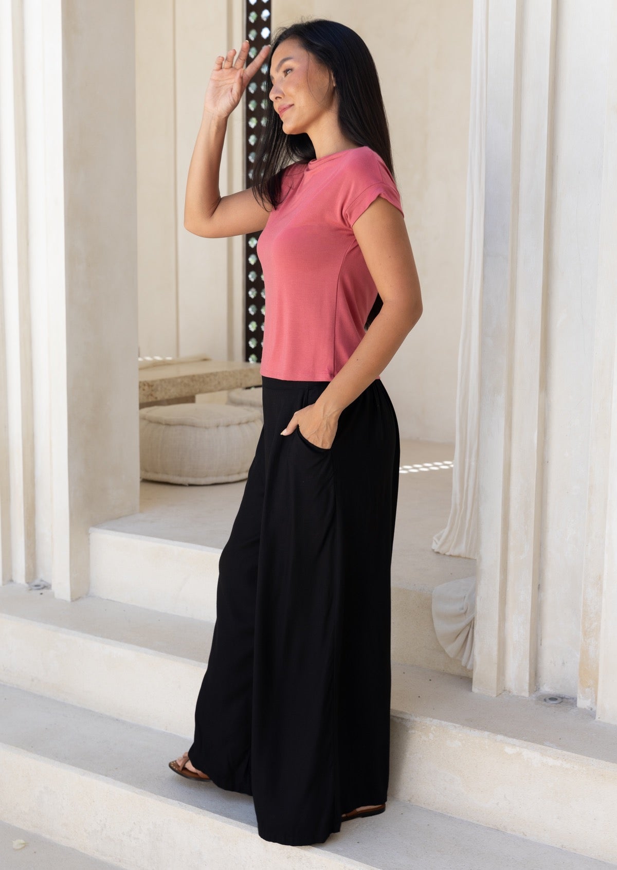 Woman in pink top paired with wide leg black rayon pants, with hand in pocket, standing on steps