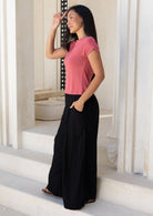 Woman in pink top paired with wide leg black rayon pants, with hand in pocket, standing on steps