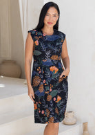 Woman wearing a sleeveless dress with a black based floral print, with one hand in front pocket
