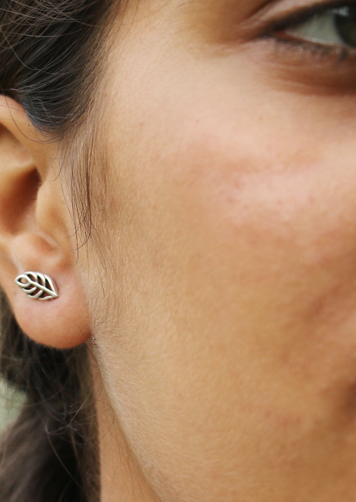 Close up image of a woman wearing a leaf cutout sterling silver studs with butterfly backs