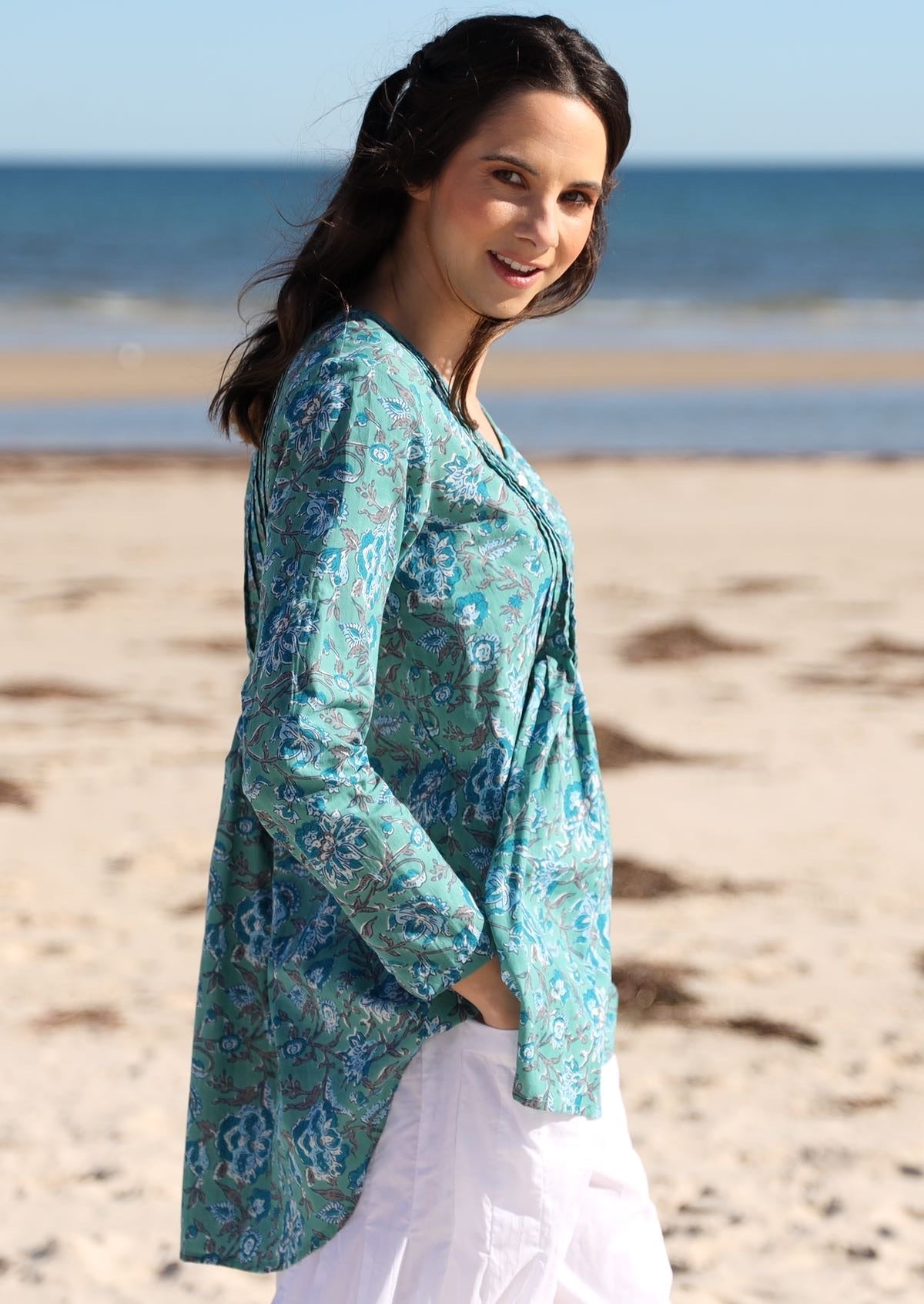 Side post of model wearing cotton long sleeve top with multiple small pleats at the front and back