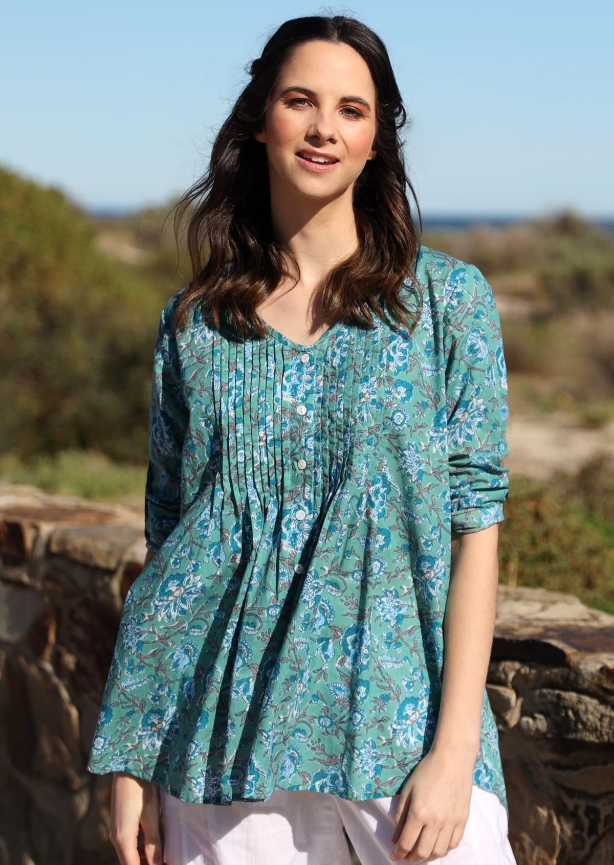 Woman poses in cotton long sleeve button through top with small pin tucks across chest in indian floral print on aqua blue base.