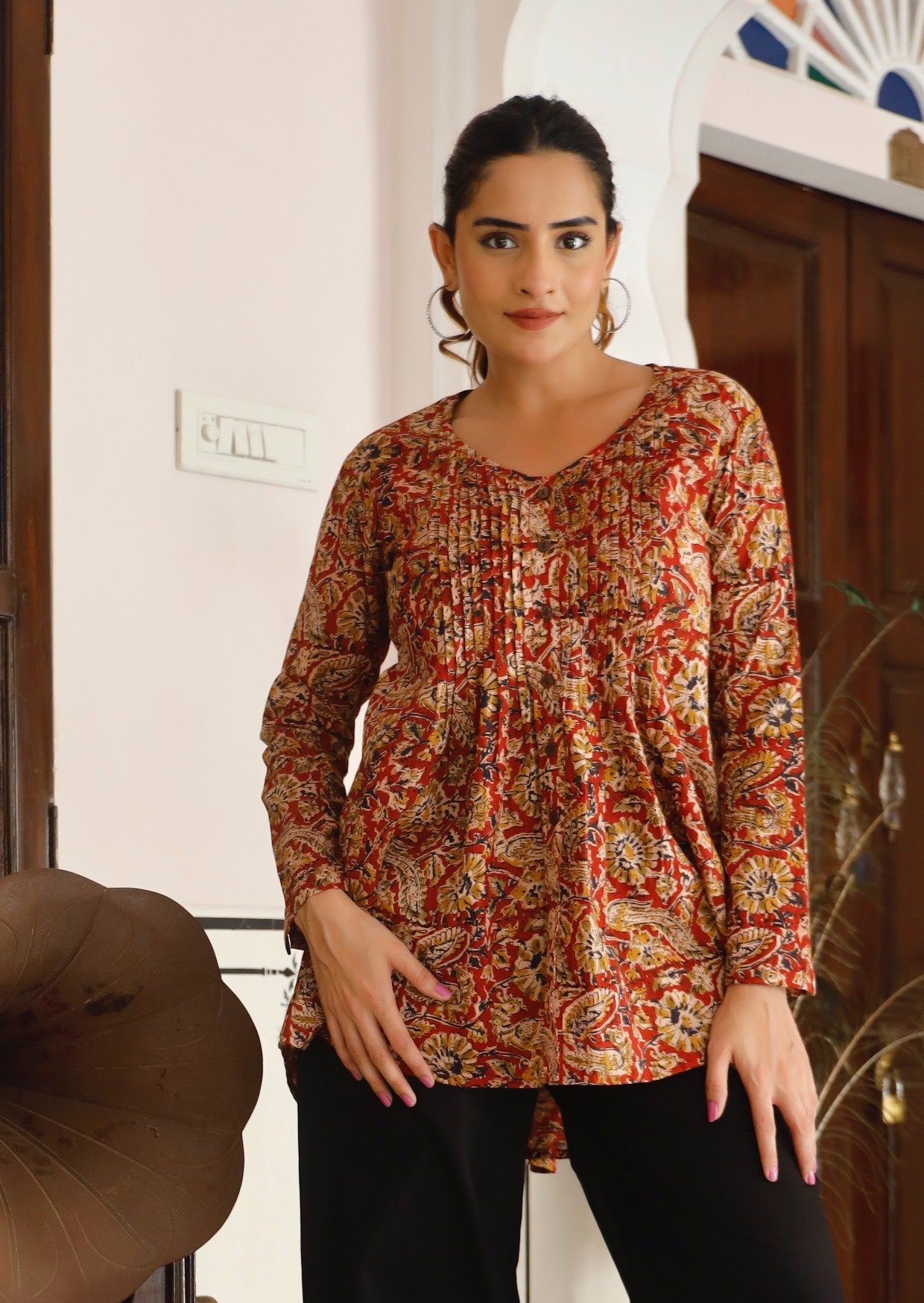 Model poses in long sleeve button through top with V-neckline and small pin-tucks across chest that leads into flared base.