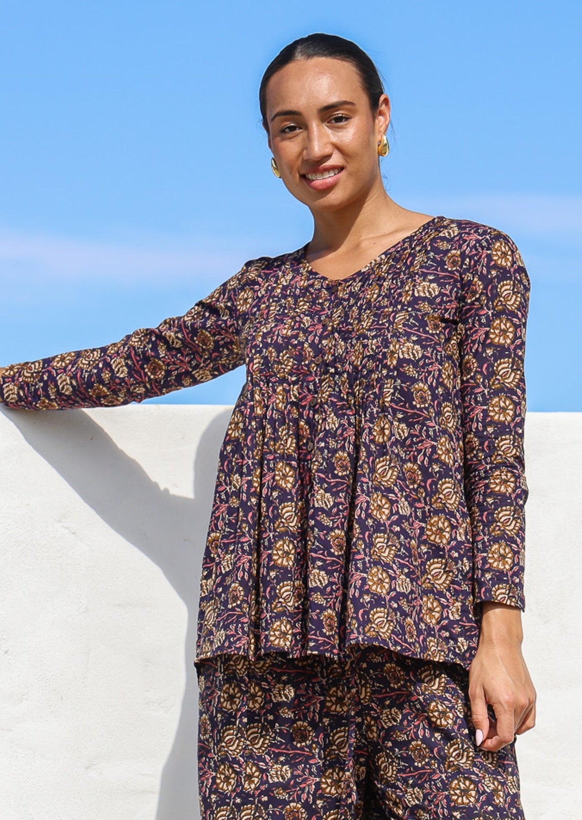 Woman in cotton long sleeve button through top with small pin tucks across chest in dark purple based floral print.