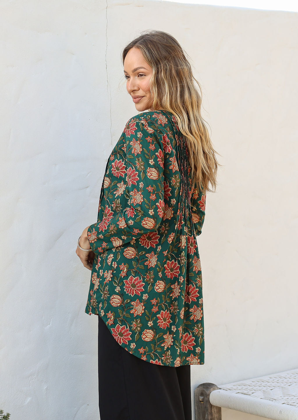 Woman wearing a green floral cotton long sleeve shirt with pin tucks across the back of the bodice, the back of shirt is longer than front