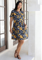 Woman stands with hand in pocket wearing a 100% cotton relaxed fit dress with round neckline and short sleeves in black based retro floral print