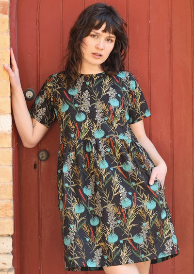Model wears Mabel Dress Thistle black base cotton with botanical print, high round neckline, t-shirt sleeves, an empire waistline and hidden side pockets | Karma East Australia