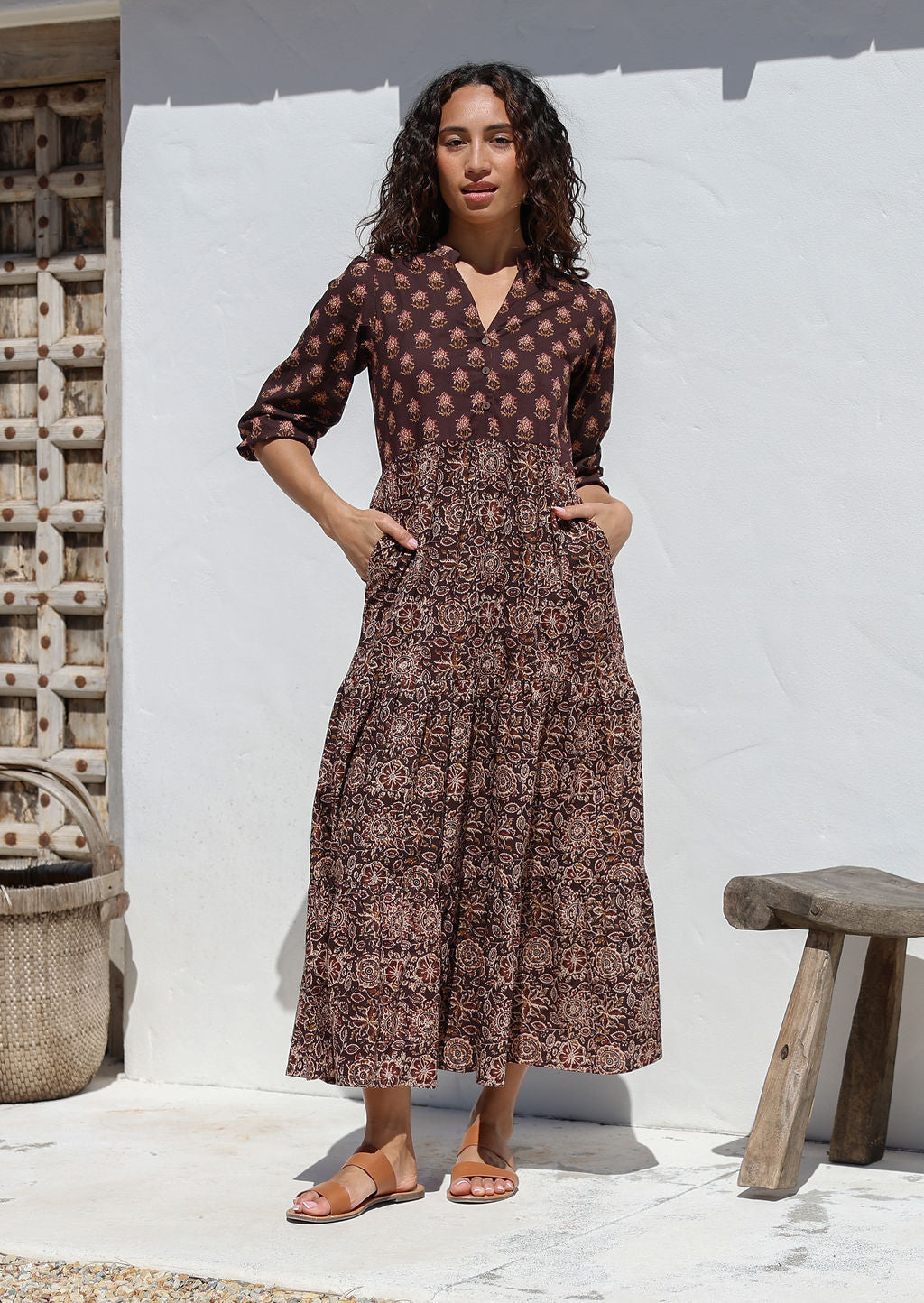 Woman wearing a brown Indian Cotton maxi dress standing against a white wall with hands in pockets 