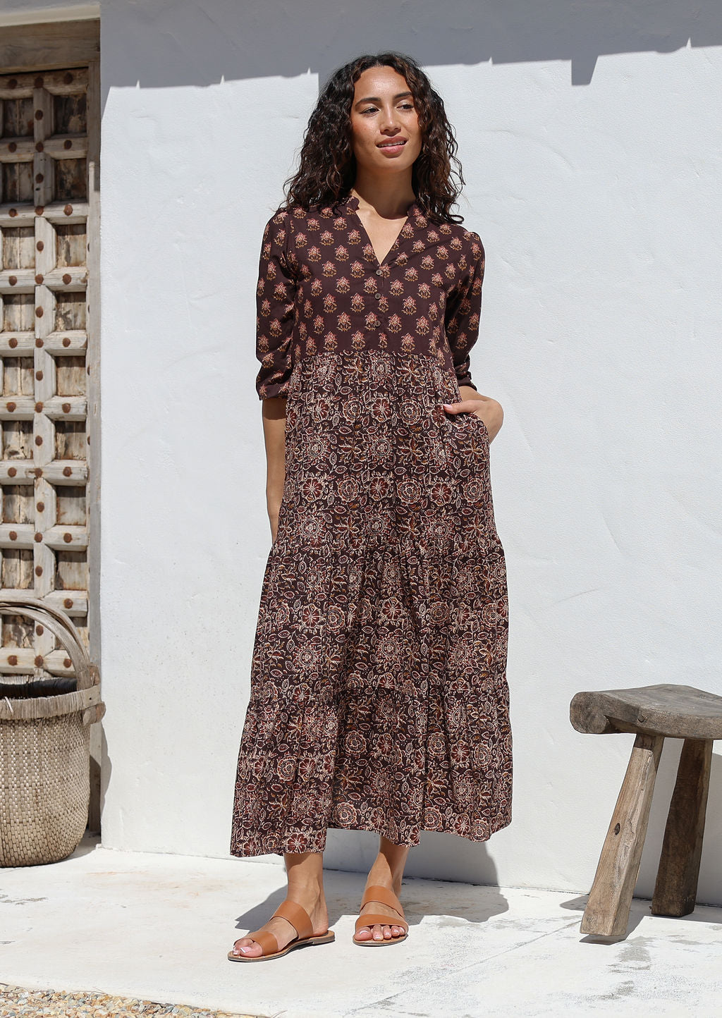 Woman wearing a brown floral Indian Cotton maxi dress standing against a white wall with hands in pockets 