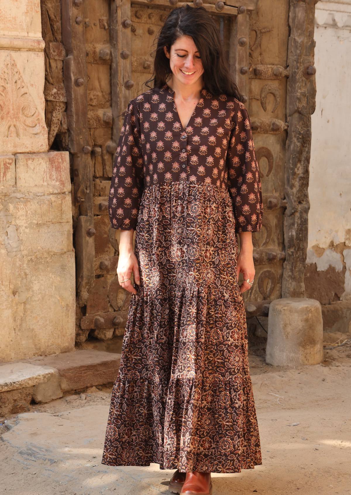Model wearing a cotton three tiered maxi dress with combination of two floral prints on earthy brown base, 3/4 sleeves and buttoned bodice.