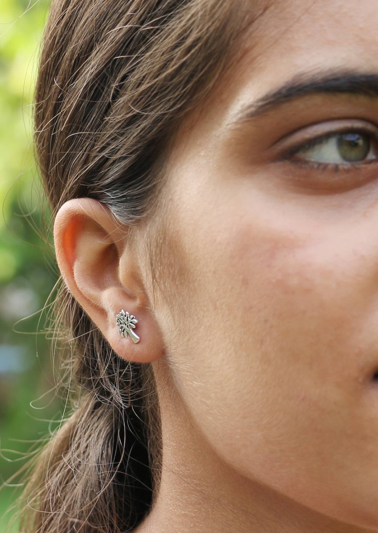 Woman with green eyes wearing a sterling silver stud in mango tree shape with green blurred background 