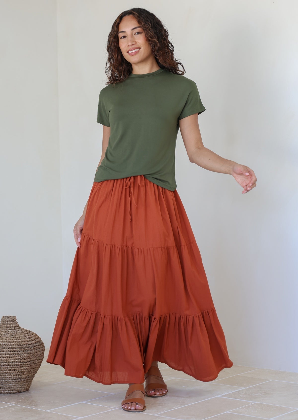 Woman wearing a green top and rust shade skirt with elasticated waistband standing against a white background